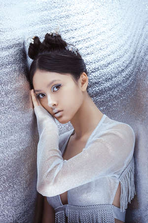 Creative art make-up and hairstyle. Portrait of asian young woman. Beautiful young model Japanese style girl in silver urban clothes with conceptual hairstyle and make-up against silver background looking at camera.の写真素材