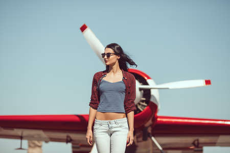 Pilot woman next to propeller plane outdoors in sunny day. Attractive young multi-racial Asian...