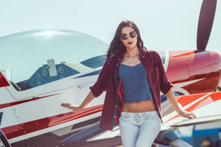 Pilot woman standing at cabin plane outdoors in sunny day. Attractive young multi-racial Asian...