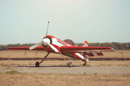 Red retro sport airplane stands on grass against a blue skyの写真素材