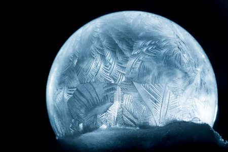 Winter background. Frozen soap bubble close-up. For Christmas and New Year Holidays exclusive backdrop. Shiny ice patterns on ball of soap against black background.の写真素材