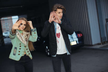 Couple hiding faces from paparazzi outdoors at parking. Fashion young couple in rock style. Pretty girl and handsome man shielding their faces from photographersの写真素材