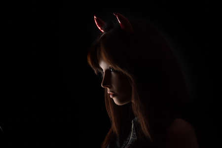 Sexy brunette girl wearing a halloween costume of a devil. Beautiful mixed race Caucasian Asian young girl posing against black background in studio. Silhouette portrait.の写真素材