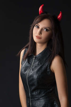 Sexy brunette girl wearing a halloween costume of a devil. Beautiful mixed race Caucasian Asian young girl posing against black background in studio.の写真素材