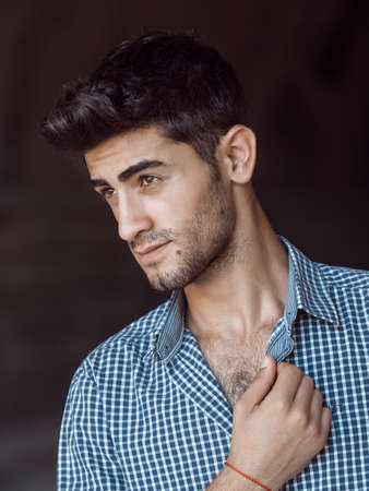Portrait of happy young man with facial hair agaist dark background looking away. Handsome man wearing t-shirt outdoorsの写真素材
