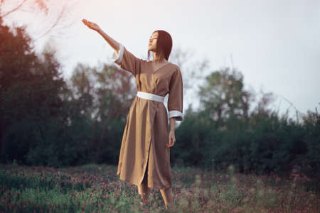 Asian woman wearing traditional japanese kimono outdoors in park. Stylish japanese model posing outdoors in fashionable dress. Young sensual girl standing on flower field in full length with closed eyesの写真素材