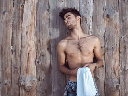 Tired athlete after workout session resting outdoors. Exhausted young handsome, muscular young worker shirtless outdoor. Handsome man after workout or nad work outdoors agaist wooden fence.の写真素材