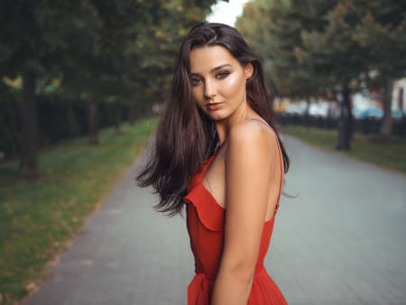 Fashion sensual woman portrait. Outdoor photo of attractive brunette model in red dress. Gorgeous brunette girl portrait in summer sexy red dress against evening city street. Shallow DOFの写真素材