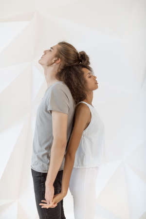 Happy loving couple standing back to back with closed on white polygon background. Young couple in love hug each other indoors. Shot of a passionate young people in love isolated over white background. Calmness and relax, family therapy.の写真素材