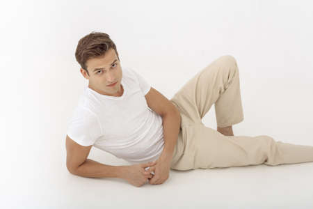 Young casual man looking pensive while lying down on white background. Guy looking at camera in...