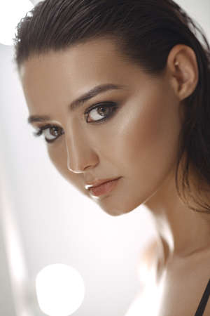 Beautiful young woman with clean fresh skin and perfect make-up looking at camera agaist white lights bokeh background. Facial treatment . Cosmetology , skin care, beauty and spa concept. Gorgeous slim mixed race Caucasian Asian girl with big eyesの写真素材