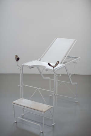 Old style chair for women diagnosis agaist white wall. Gynie exam table in museum.の写真素材