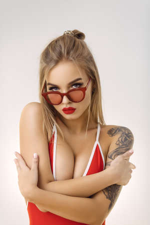 Young sexy blonde woman posing in fashionable swimsuit and sunglasses. Girl with an ideal body. Studio shot. Attractive female in bikini looking at the camera. Close up portrait.の写真素材