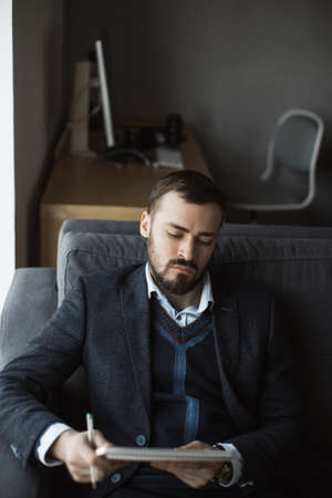Confident concentrated handsome bearded businessman in a trendy suit reading important ideas in a...