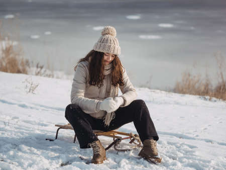 Winter woman playing in the snow, making snowball, having fun outside on sunny winter day. Beautiful joyful multicultural Asian Caucasian girl sitting on the sledge outdoors during winter vacations.の写真素材