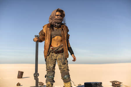 Post-apocalyptic woman with weapon outdoors. Young slim girl warrior in shabby clothes holding sword...