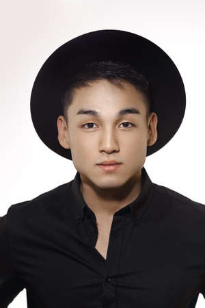 Close-up portrait of a handsome Asian man with short haircut posing in a trendy black hat and black...