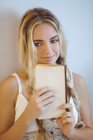 Beautiful smiling young woman enjoying a book sitting on a bed at home. Close-up portrait of happy thinking girlの写真素材