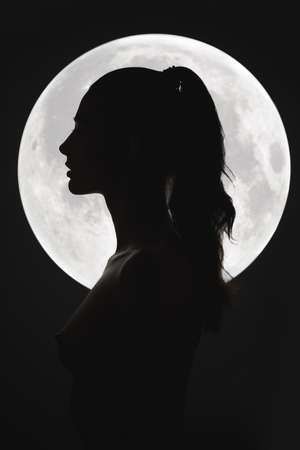 Fine art fashion studio portrait of a nude sensual woman at night sky and a full moon.Profile of stunning face, perfect body, slim figure, beautiful breast. Young adult mixed race Asian Caucasian model seductive look. Art of eroticaの写真素材
