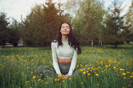 Fit woman resting on green dandelion meadow against forest. Training and resting outdoor. Healthy...