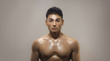 Portrait of an athletic muscular Asian man standing on a grey background. Attractive confident young man looking at the camera. Male Fashion shot, muscular Asian guyの写真素材