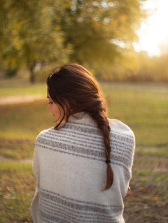Portrait of a romantic brunette woman standing in the park at fall on a sunny day. The back view of a tender beautiful woman in autumn outdoor at sunset.の写真素材