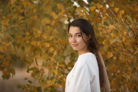 Portrait of a romantic brunette woman standing in the park at fall on a sunny day smiling and looking to the camera. The face of a happy beautiful woman in autumn outdoor at sunset.の写真素材