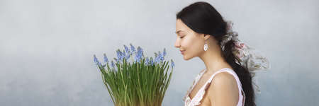 Beautiful young woman smelling bouquet of spring flowers with closed eyes. Sensual romantic mixed race female florist with mouse Hyacinth Muscari in hands. Life lover, zero waste, spring mood concept.の写真素材