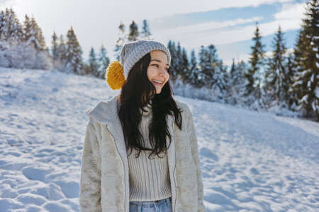 Portrait young adult woman in casual warm clothes against snowy winter background during vacations outdoorsの写真素材