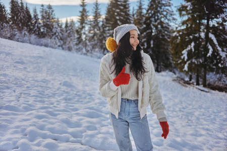 Woman in Winter Clothes Thumbs Up in Front of Mountain Forest Outdoorsの写真素材