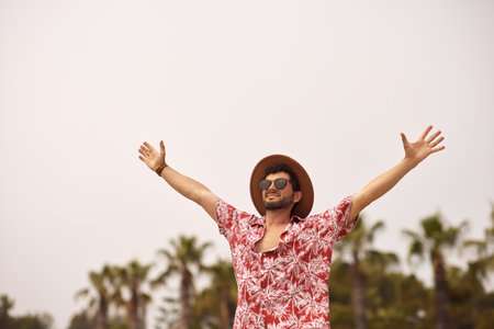 Happy Beach Man With Raised Hands Outdoors Against Palm Trees on the Background During Summer Vacationsの写真素材