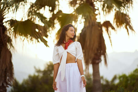 Woman in Elegant Beach Outfit Outdoors Against Palm Trees on the Background During Summer Vacations