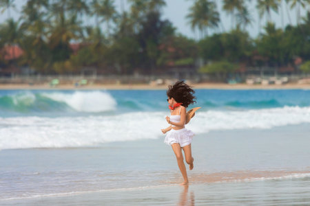 A slender girl in white clothes runs along the beach against the background of the sea.の写真素材