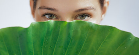 Close-up Face of Young Woman with Perfect Skin, Behind Green Leafの写真素材
