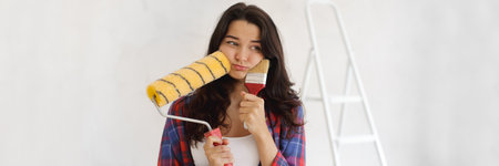 Pensive Woman Holding Paint Roller and Brush for DIY Home Renovation Bannerの写真素材