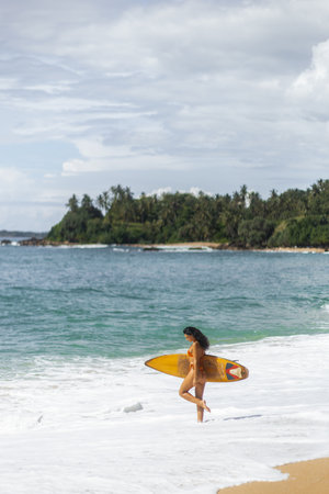 Surfer Woman Walking on Tropical Beach with Surfboardの写真素材