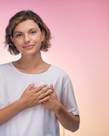 Woman with Hands on Heart Showing Gratitude Against Gradient Backgroundの写真素材