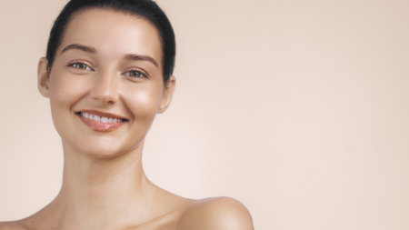 Smiling Woman with Natural Makeup and Radiant Skin Against Beige Backgroundの写真素材
