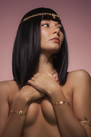 Elegant Woman with Gold Jewelry Posing Against Pink Backgroundの写真素材