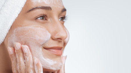 Happy Woman with Towel Cleansing Face with Foaming Cleanser in Skincare Routineの写真素材