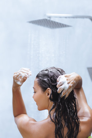 Woman Lathering Hair With Shampoo Under a Relaxing Rainfall Showerの写真素材