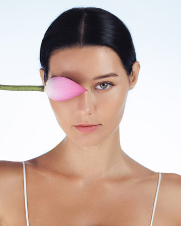 Serene Woman With Pink Lotus Flower Covering One Eye in Minimalist Setting