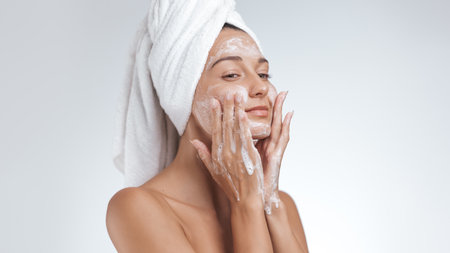 Woman Gently Washing Face with Foam, Towel Wrapped Hair, Skincare Conceptの写真素材