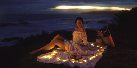 Romantic Evening Picnic By The Ocean With Fairy Lights And Elegant Womanの写真素材