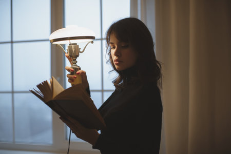 Young Woman Reading A Book By Lamp Light In A Cozy Evening Setting
