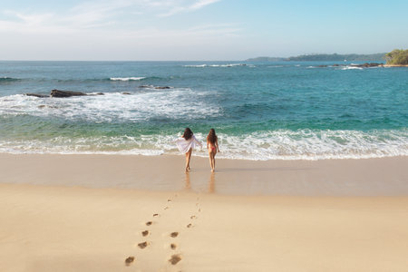 Women Walking Towards the Ocean on a Serene Beachの写真素材