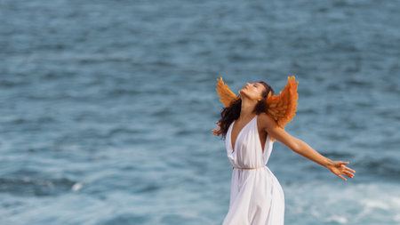 Fantasy Angelic Woman With Golden Wings Embracing Freedom by the Seaの写真素材