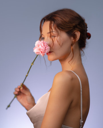 Elegant Woman Savoring the Scent of a Pink Flower in Soft Studio Lightの写真素材