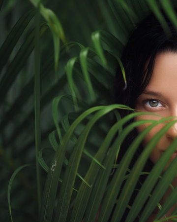 Captivating Close-Up of Woman Eye Hidden Behind Tropical Leavesの写真素材