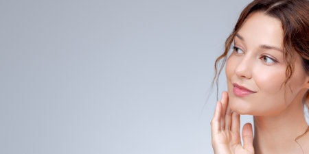 Graceful Beauty Banner with Young Woman Touching Face Against Soft Grey Backgroundの写真素材